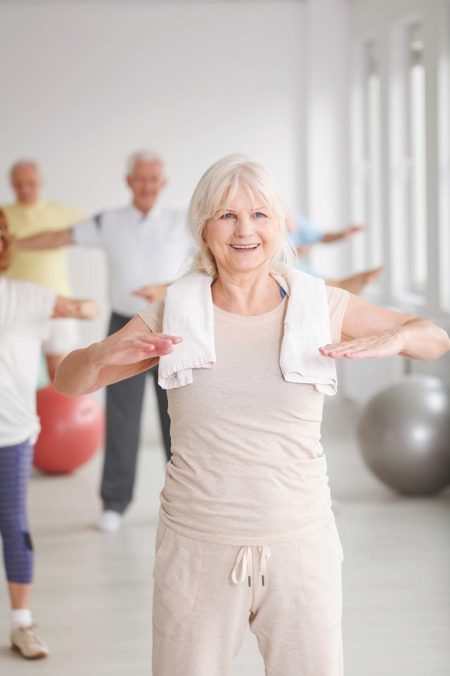 Smiling elder lady with towel stretching at the gym