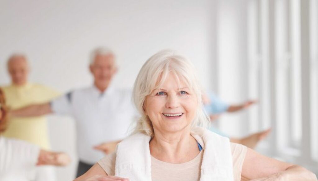 Smiling elder lady with towel stretching at the gym