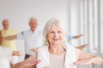 Smiling elder lady with towel stretching at the gym