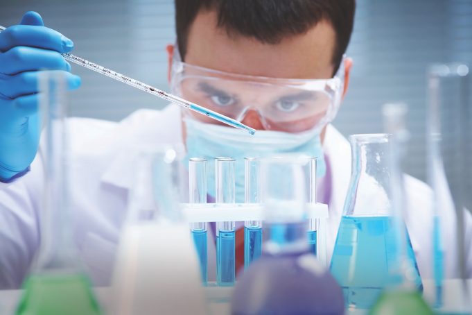 Survive and Strengthen Investigator checking test tubes. Man wears protective goggles