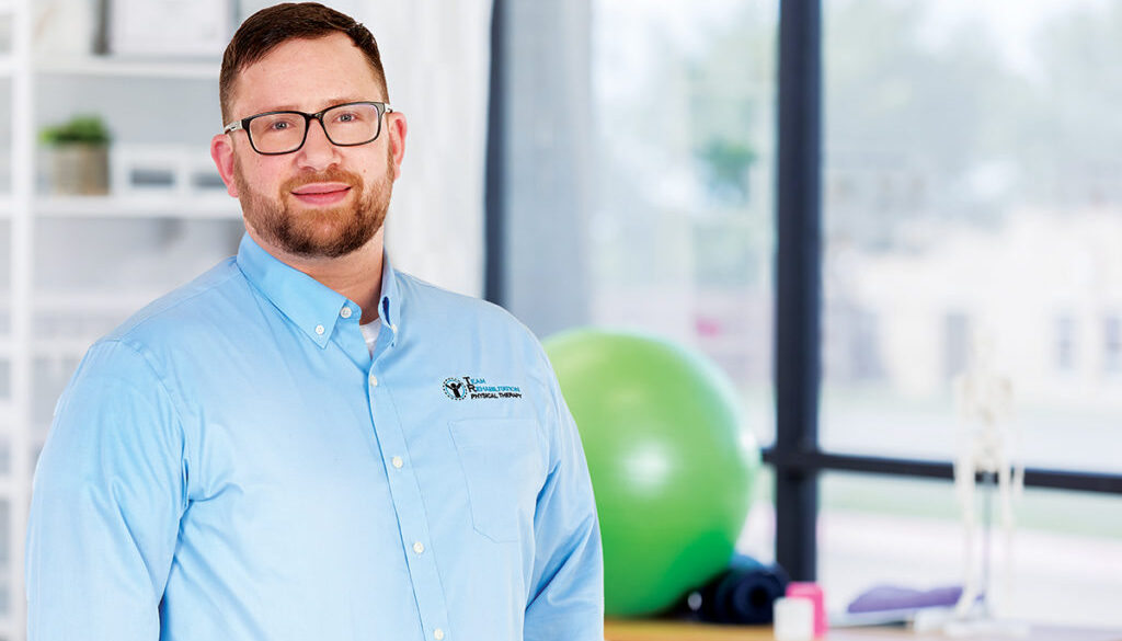 Cheerful mid adult physical therapist smiles confidently in a gym. She is holding hand weights.