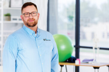 Cheerful mid adult physical therapist smiles confidently in a gym. She is holding hand weights.