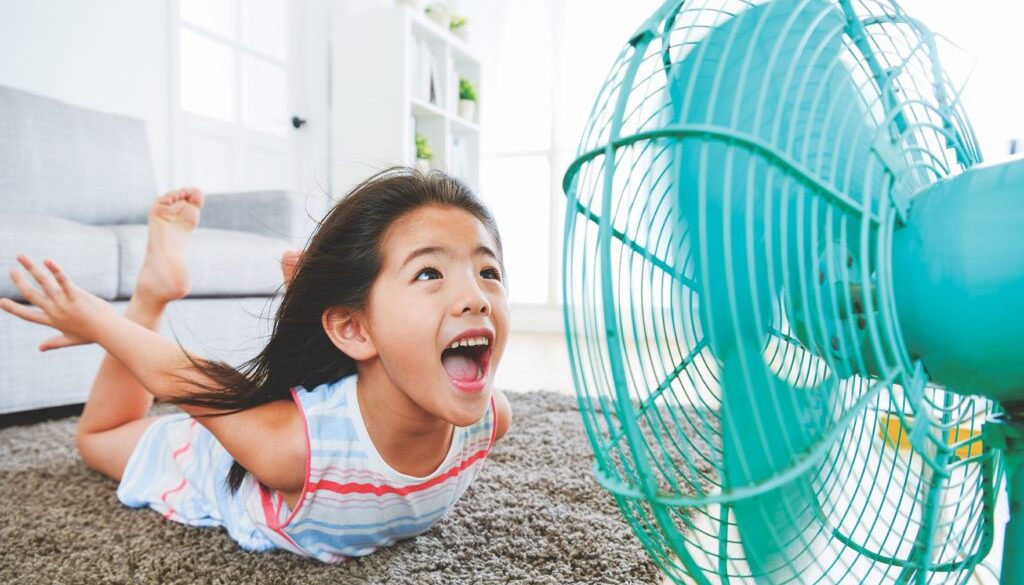 sweet beautiful little children lying down on living room floor and face to electric fan enjoying cool wind with flying posing with selective focus photo.