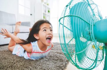 sweet beautiful little children lying down on living room floor and face to electric fan enjoying cool wind with flying posing with selective focus photo.