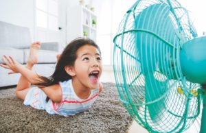 Don’t Sweat The Heat sweet beautiful little children lying down on living room floor and face to electric fan enjoying cool wind with flying posing with selective focus photo.