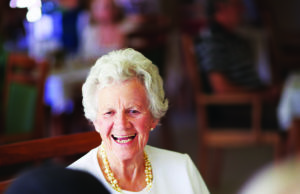Living Well A cheerful old lady sitting with her elderly friends at lunch at their nursing home