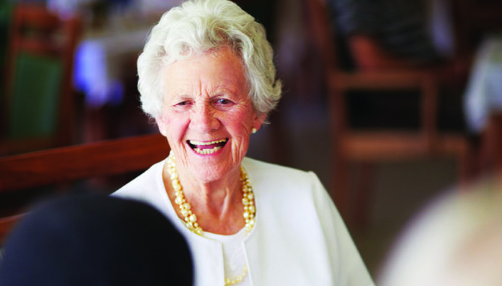 A cheerful old lady sitting with her elderly friends at lunch at their nursing home