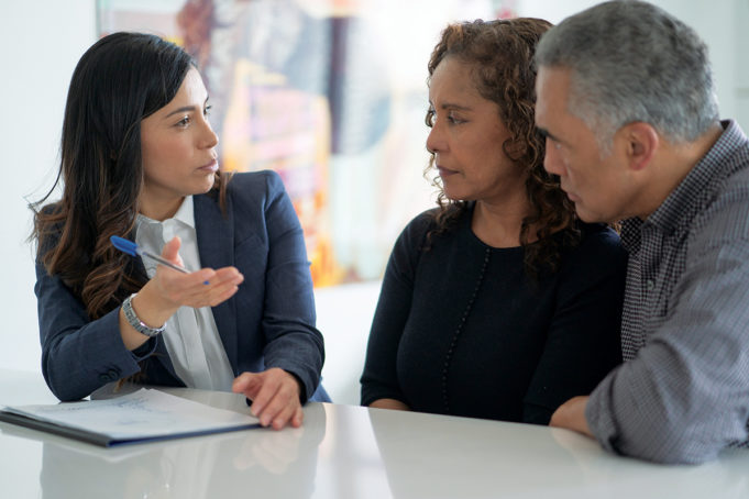 Are You Fully Prepared For Your Golden Years? An adviser meets with a mixed race middle-aged couple to discuss their life insurance or financial needs. The couple is dressed casually and the adviser is in a suit. They are seated around the clients kitchen table.