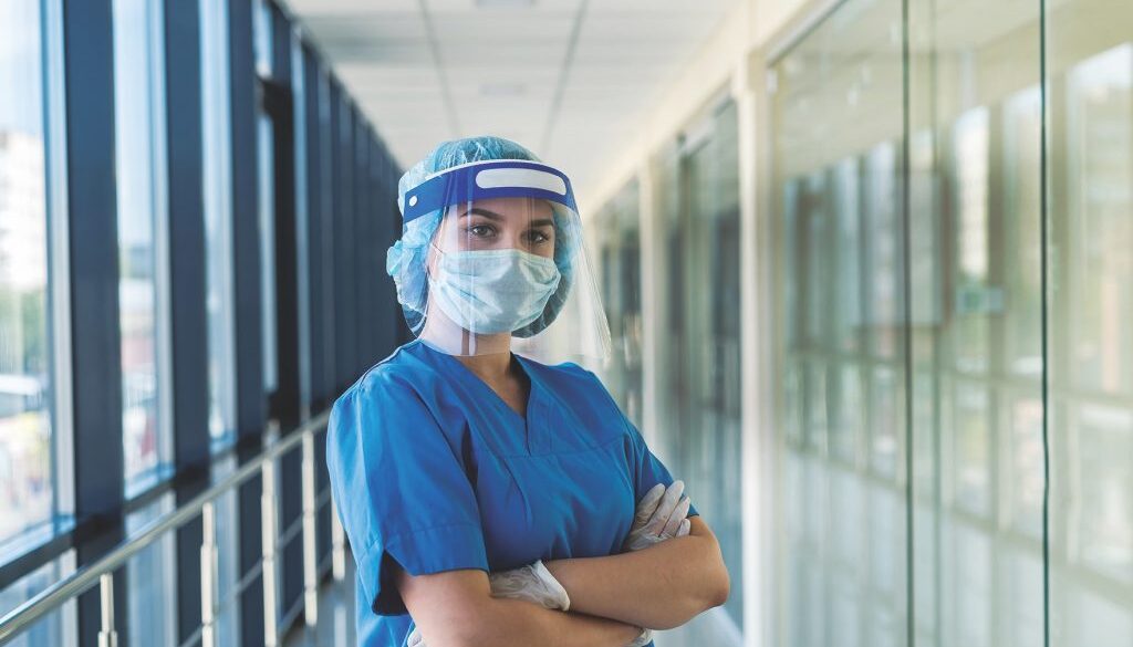 portrait of a young nurse in a blue uniform and a protective shield to protect against a new dangerous virus covid19