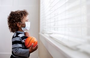 The ‘Other’ Pandemic A young boy looking out the window wearing a protective facemark while seeking protection from COVID-19, or the novel coronavirus, by sheltering in place in his home.