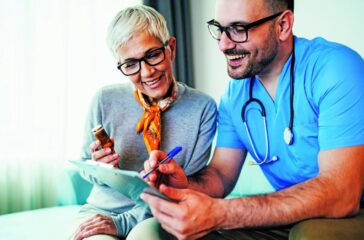Young smiling doctor is consulting a modern senior woman - patient, on the visit at home