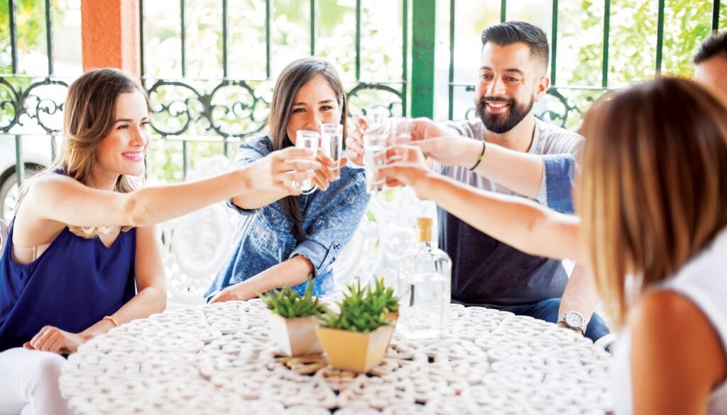 Five good looking Latin friends having fun in a Mexican party drinking tequila shots outdoors