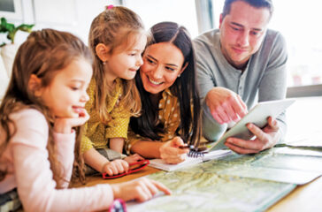 Young happy family with two children and tablet preparing for holidays at home.