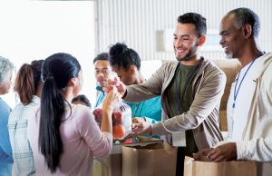 Ameris Bank Commemorates 50 Years of Giving Back Young woman hands a bag of fruit to a young male food bank volunteer. The volunteers are receiving donations from their community to benefit a food bank.