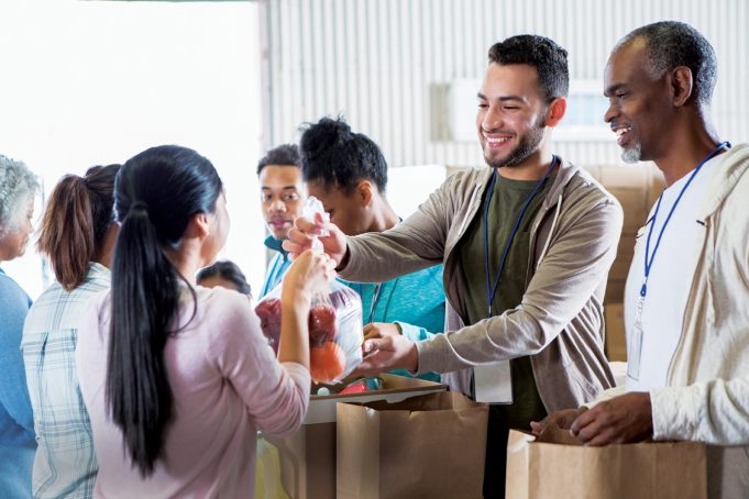 Ameris Bank Commemorates 50 Years of Giving Back Young woman hands a bag of fruit to a young male food bank volunteer. The volunteers are receiving donations from their community to benefit a food bank.