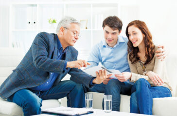 Young Couple Meeting With Senior Financial Advisor presenting new bank offers and investments on digital tablet PC. Senior Financial Advisor pointing with hand to some new offers.