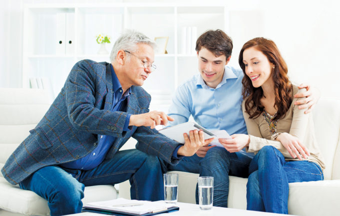 An Agent Can Make All The Difference Young Couple Meeting With Senior Financial Advisor presenting new bank offers and investments on digital tablet PC. Senior Financial Advisor pointing with hand to some new offers.