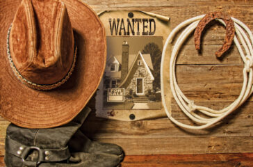Very rusty old horseshoe symbol of luck and lasso hanging on a wooden wall cowboy hat and boots and blank sheet of paper with place for text
