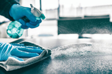Cleaning home table sanitizing kitchen table surface with disinfectant spray bottle washing surfaces with towel and gloves. COVID-19 prevention sanitizing inside.