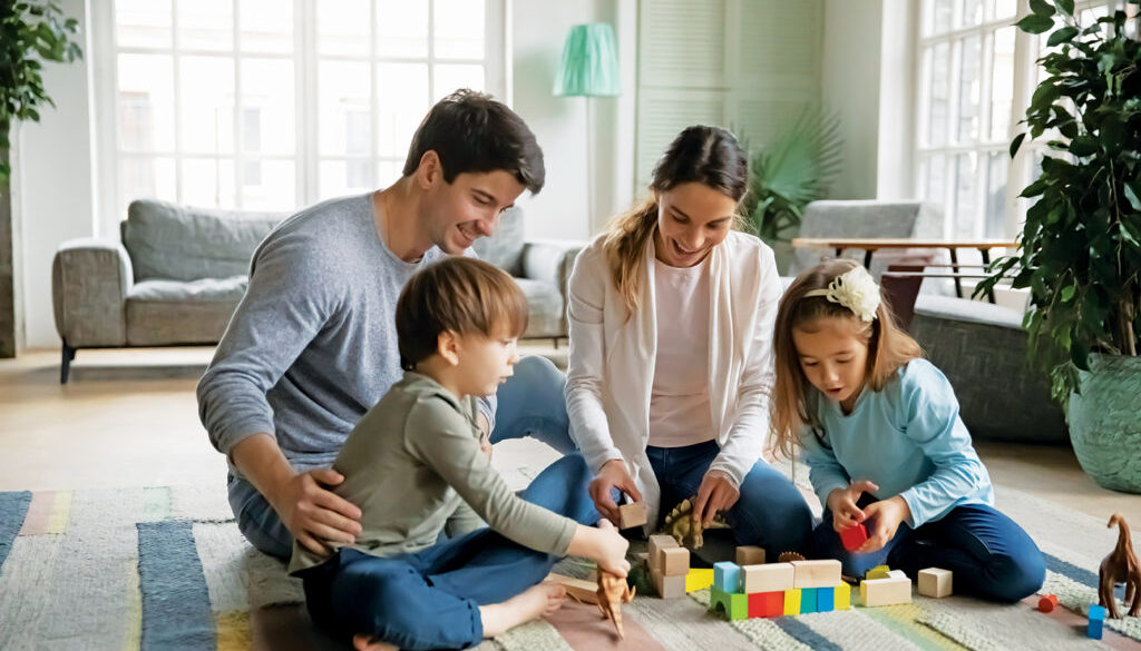 Affectionate caring young parents sitting on floor carpet with little joyful children siblings, playing toys together at home. Happy caucasian family with small kids involved in weekend game indoors.