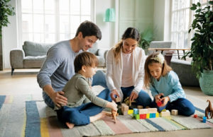 Siblings In Foster Care are Better Together Affectionate caring young parents sitting on floor carpet with little joyful children siblings, playing toys together at home. Happy caucasian family with small kids involved in weekend game indoors.