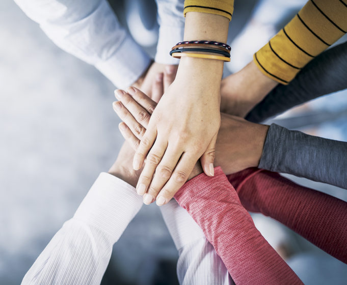 Supporting Business Owners & The Community Close up top view of young business people putting their hands together. Stack of hands. Unity and teamwork concept.