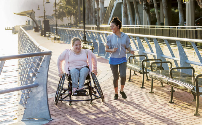 How Walkability and Movability Can Impact People, Place, and Prosperity in Cobb County Two friends exercising along a city waterfront. The young woman in the wheelchair has spina bifida. Her friend jogging beside her and talking is a mid adult Hispanic woman in her 30s.