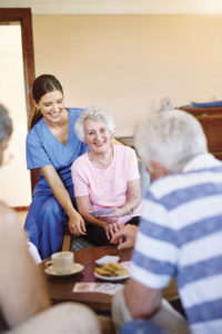 Shot of a group of happy seniors playing a card game in their retirement home while a nurse watches