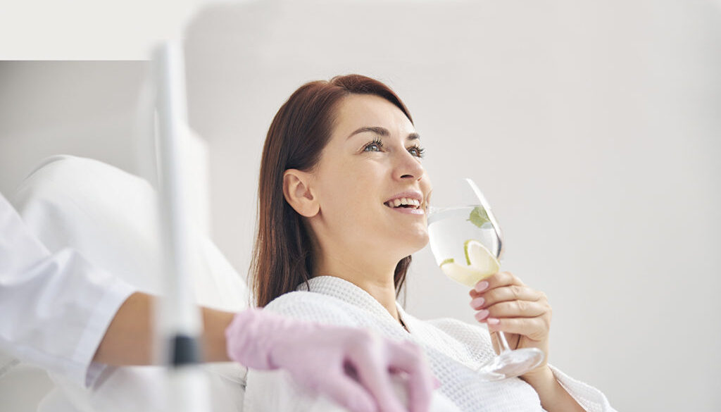 Joyous female patient drinking a healthy beverage during a medical procedure in a beauty clinic
