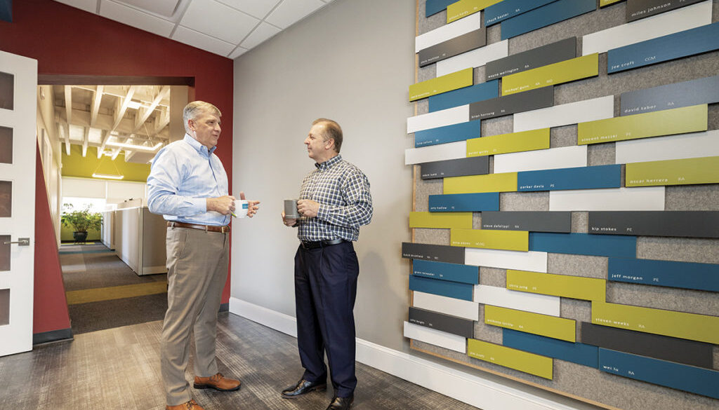 CEO Jim Croft, RA, NCARB (right); and President Mark Jackson, PE, AIA, next to the firm’s wall which displays employees’ professional accomplishments.