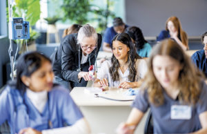 Wellstar Supports Developing Future Healthcare Professionals at Cobb Innovation Technology Academy A large group of medical students are seen sitting in rows of desk as they work in pairs on various activities. They are each dressed professionally in scrubs and are working diligently on perfecting their skills. Their professor is seen checking in on various students in the background.