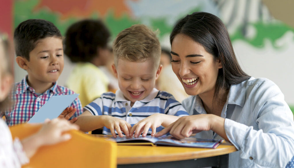 Portrait of a happy Latin American teacher reading a book with a student at the school and having fun - education concepts
