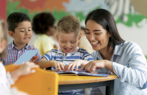A Personal Endeavor. A Community Need. Portrait of a happy Latin American teacher reading a book with a student at the school and having fun - education concepts