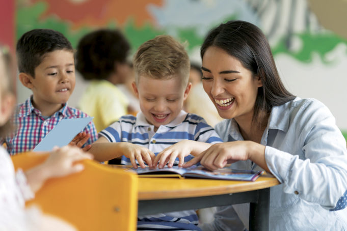 A Personal Endeavor. A Community Need. Portrait of a happy Latin American teacher reading a book with a student at the school and having fun - education concepts