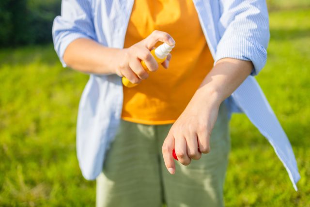Mosquito repellent. Woman using insect repellent spray outdoors. High quality photo