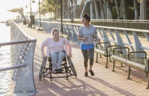 How Walkability and Movability Can Impact People, Place, and Prosperity in Cobb County Two friends exercising along a city waterfront. The young woman in the wheelchair has spina bifida. Her friend jogging beside her and talking is a mid adult Hispanic woman in her 30s.