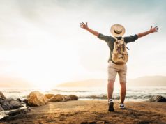 Seriously, Take A Vacation Happy man with backpack standing with arms up at the beach - Delightful tourist enjoying summer vacation by the seaside - Traveling life style and well being concept
