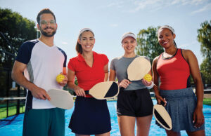 A Practical Guide To Hosting A Charity Pickleball Tournament Group of happy athletic friends playing mixed doubles in pickleball and looking at camera.